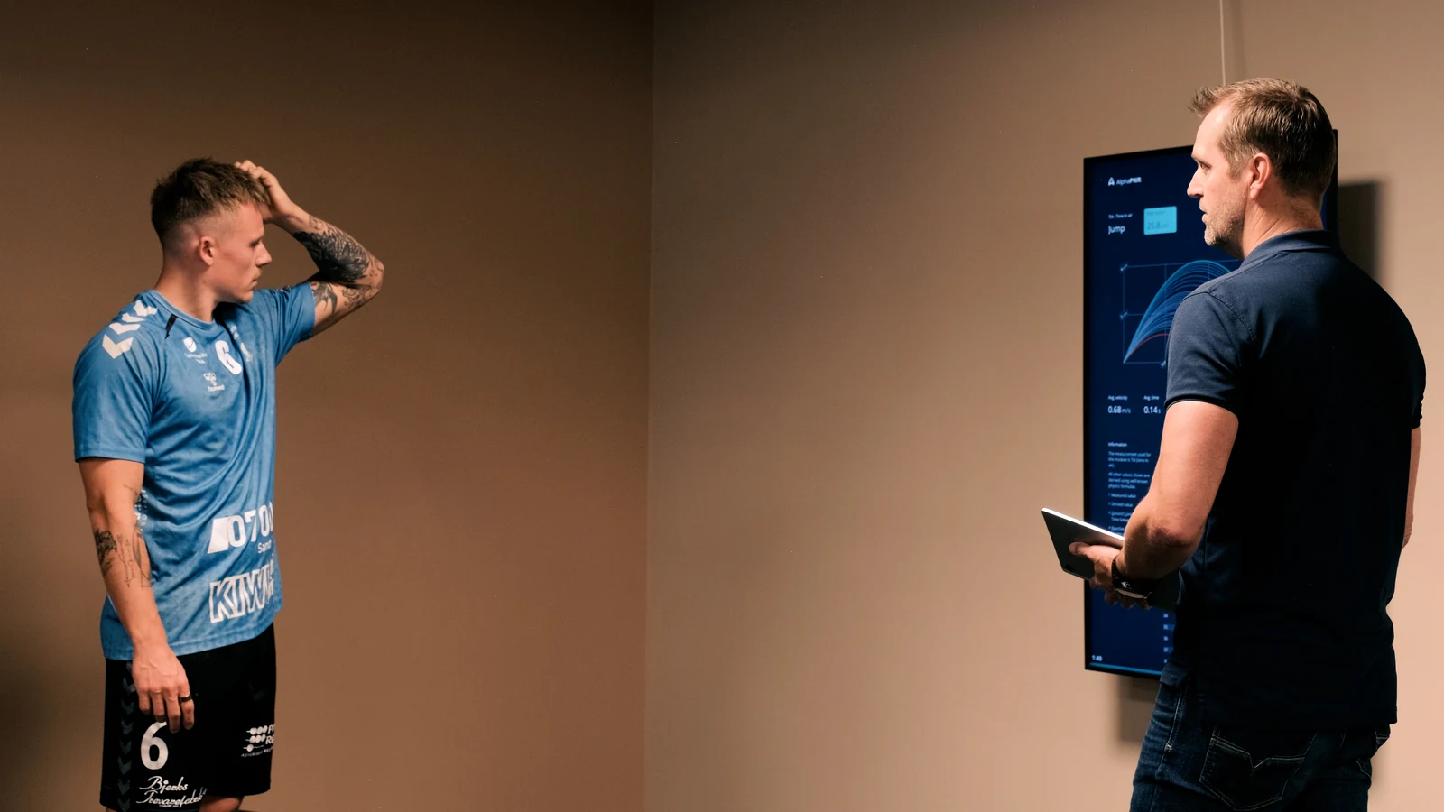 A participant and a guide holding a tablet stand beside the Alphatek display showing jump measurement curves.