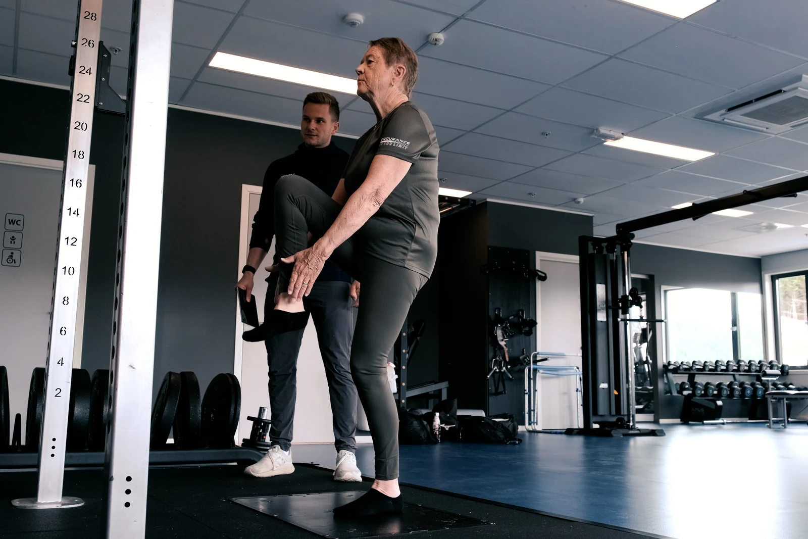 A participant stands on one leg on the Alphatek platform while a guide observes.