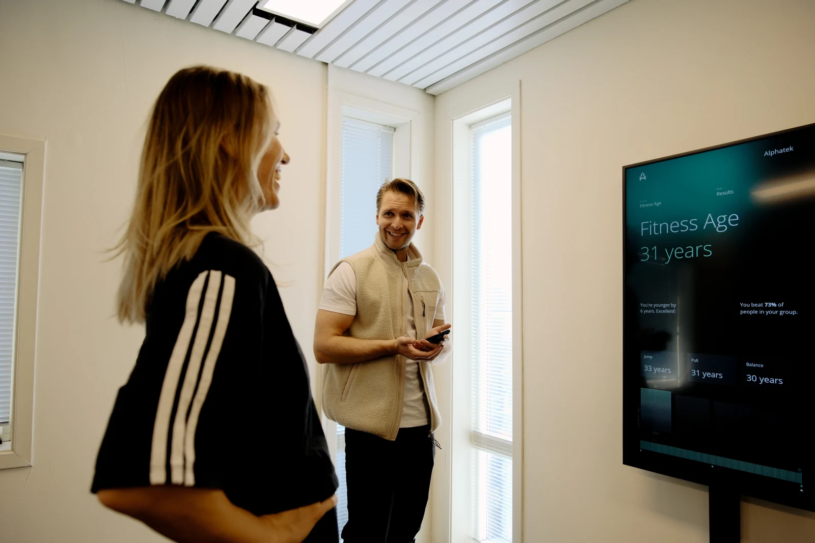 Et medlem og en trener snakker sammen ved Alphatek-skjermen som viser et Fitness Age-resultat.