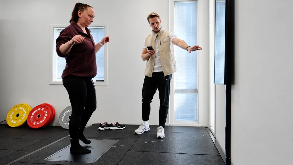 Et medlem gjennomfører en balanseaktivitet på Alphatek-plattformen mens treneren veileder.