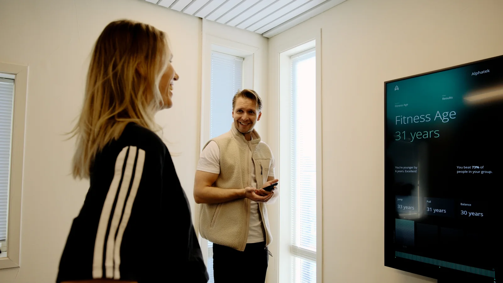 To personer snakker sammen ved Alphatek-skjermen som viser et Fitness Age-resultat.