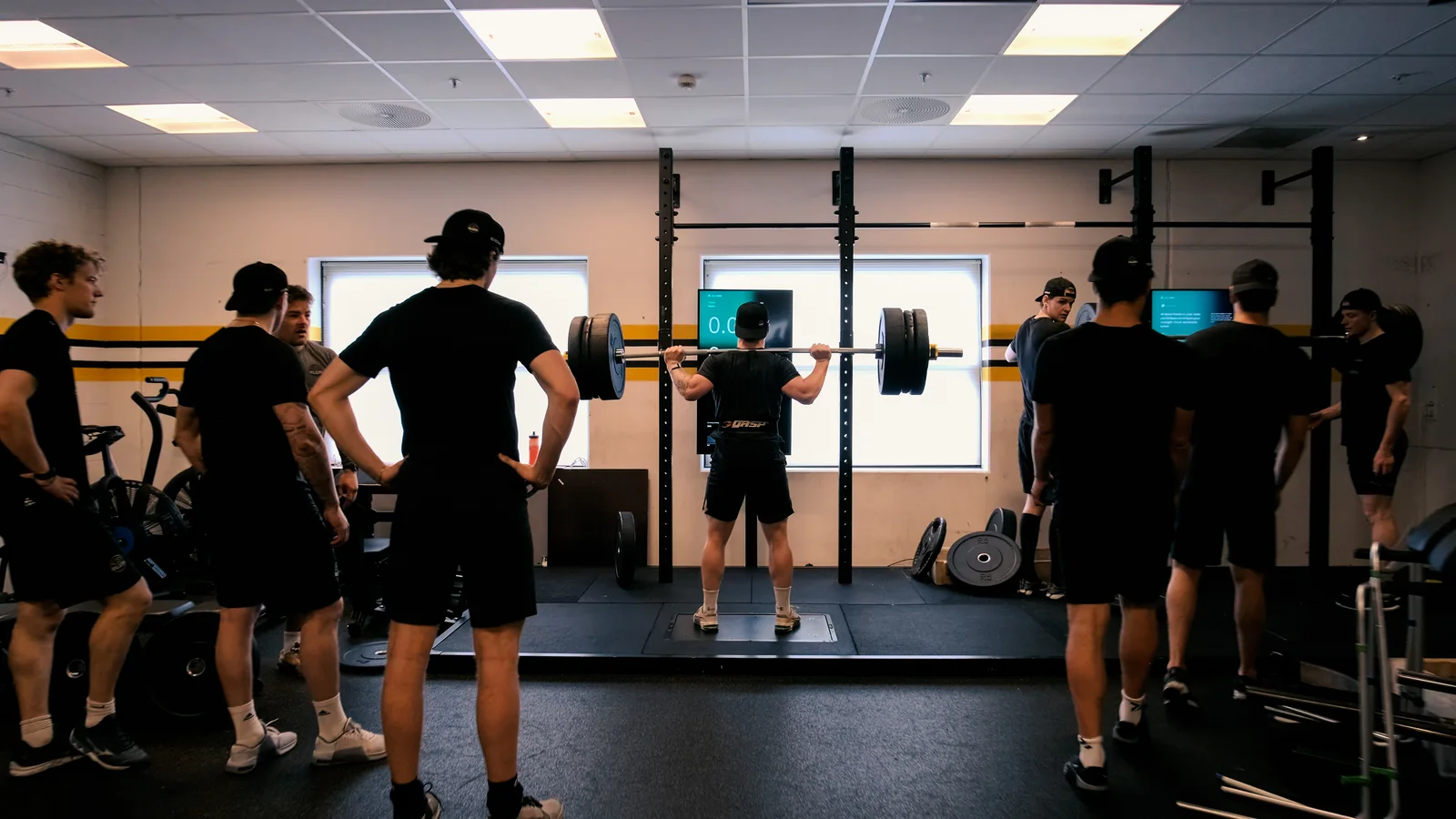 En utøver gjør knebøy på Alphatek-plattformen mens andre følger med.